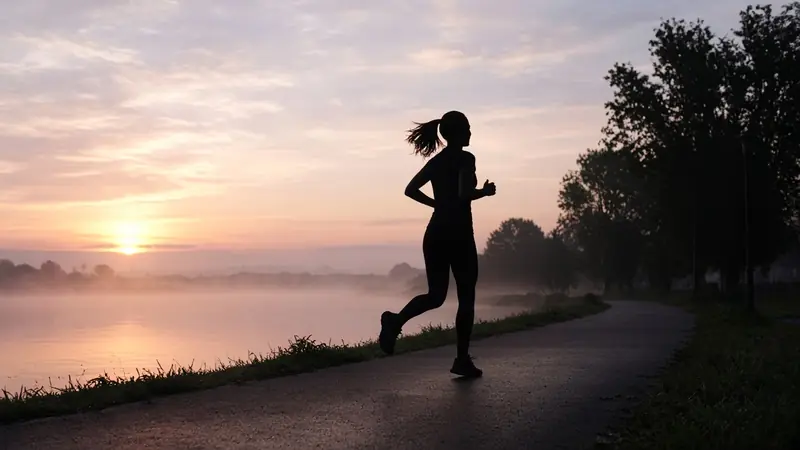 Silhouette of a person running along a waterfront path at dawn.