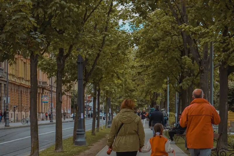 An adult and a teenager seen from behind, walking away along a tree-lined path. One carries a backpack.
