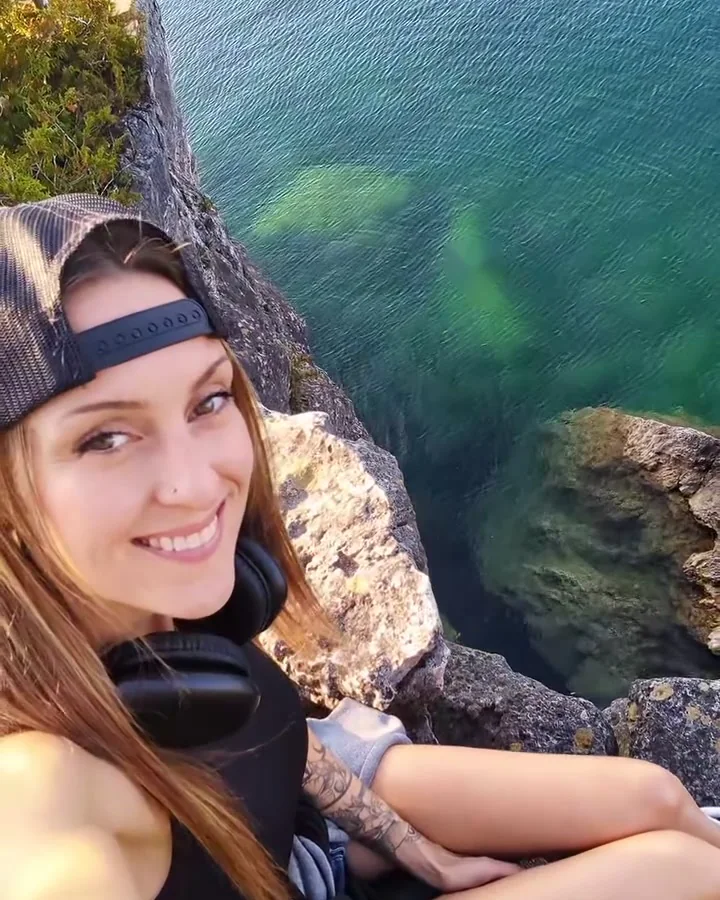 A woman smiling on a rocky cliff above clear green water